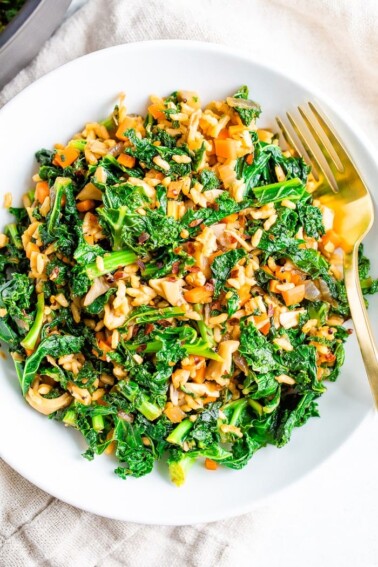 Bowl of sautéed kale, mushrooms and Spanish rice with a gold fork.