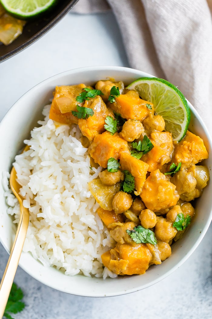 Bowl with half rice and half sweet potato chickpea curry topped with cilantro and lime.
