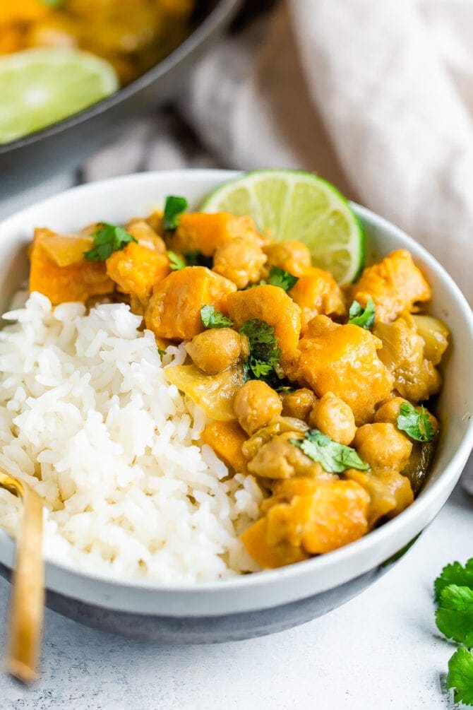 Bowl with half rice and half sweet potato chickpea curry topped with cilantro and lime.