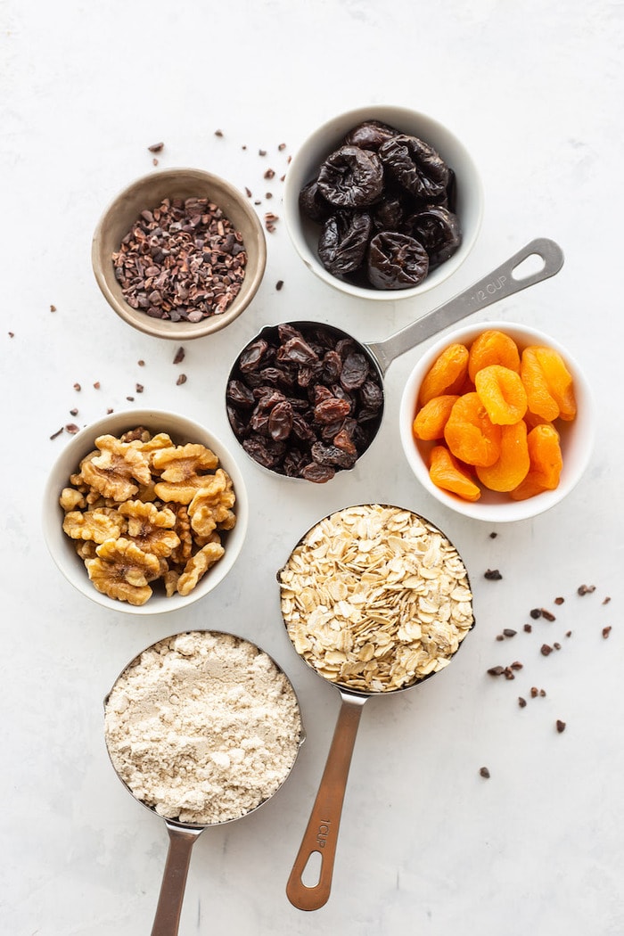 Ingredients to make fruit and nut bars in measuring cups, including oats, walnuts, and dried fruit.