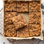 Square pan with fruit and nut bars cut into 9 slices. The middle square is sitting on top of the surrounding square pieces. The pan is sitting on a cooling rack.