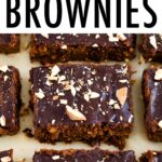 Sweet potato brownies on parchment paper topped with a chocolate ganache and chopped almonds.