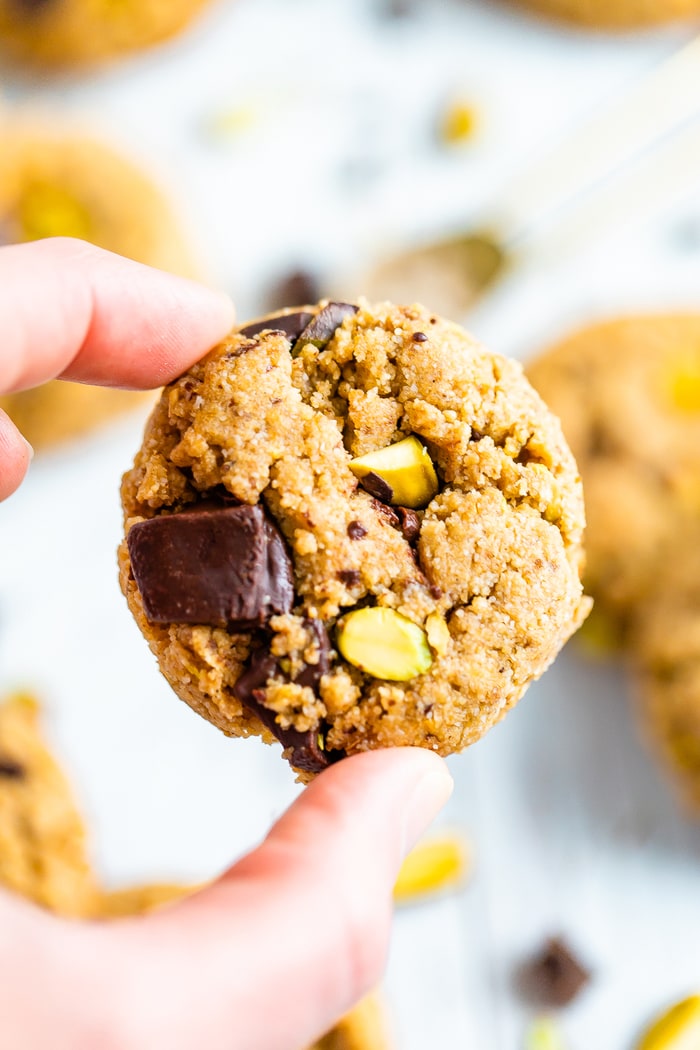 Hand holding a dark chocolate pistachio cookie.