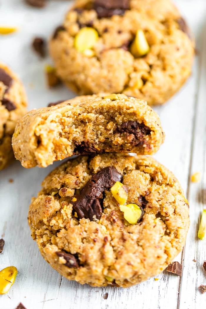 Two dark chocolate chunk pistachio cookies. One has a bite taken out of it.