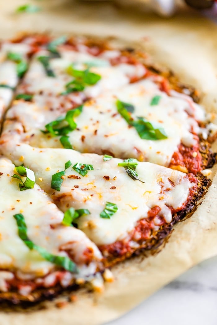 Spaghetti squash pizza on parchment paper topped with cheese, basil and red pepper flakes.