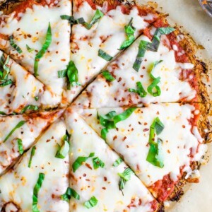 Spaghetti squash crust pizza cut into 8 slices on parchment paper and topped with basil, cheese and red pepper flakes.