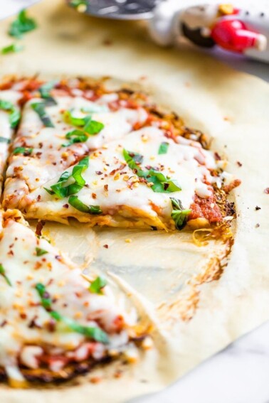 Spaghetti squash pizza crust pizza topped with fresh basil and cheese. A slice is cut out from the pizza.