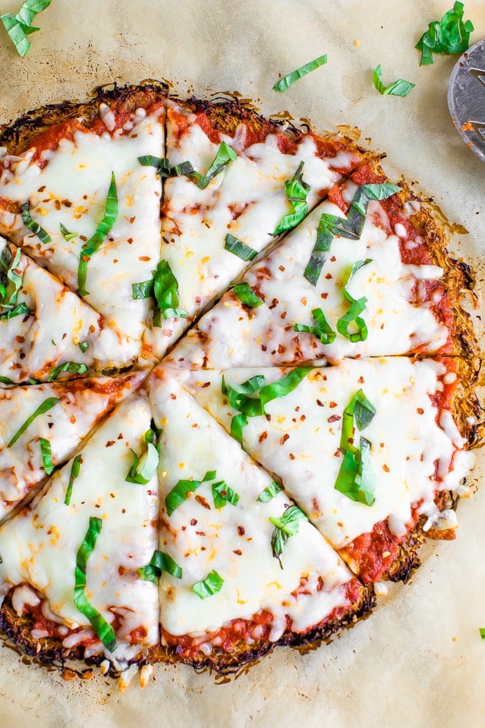 Spaghetti squash crust pizza cut into 8 slices on parchment paper and topped with basil, cheese and red pepper flakes.