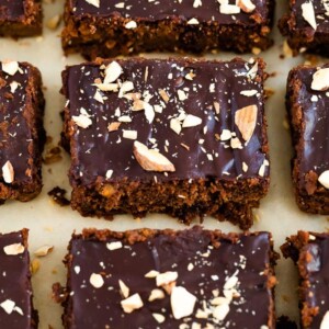 Sweet potato brownies on parchment paper topped with a chocolate ganache and chopped almonds.