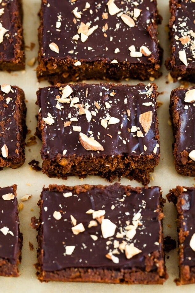 Sweet potato brownies on parchment paper topped with a chocolate ganache and chopped almonds.