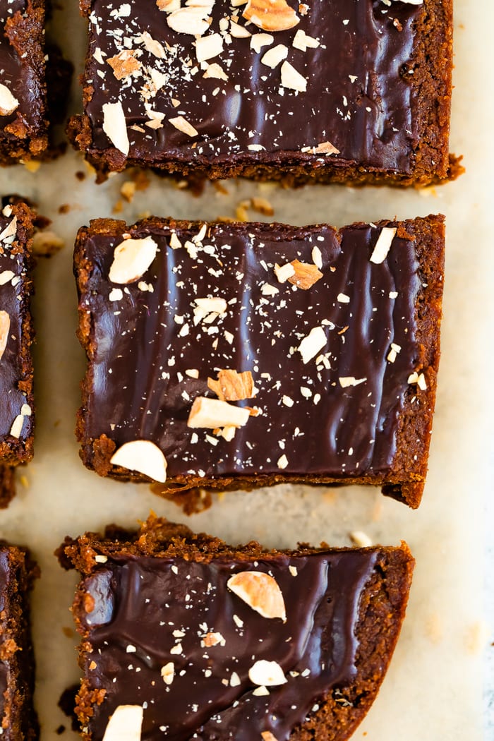 Sweet potato brownies on parchment paper topped with a chocolate ganache and chopped almonds.