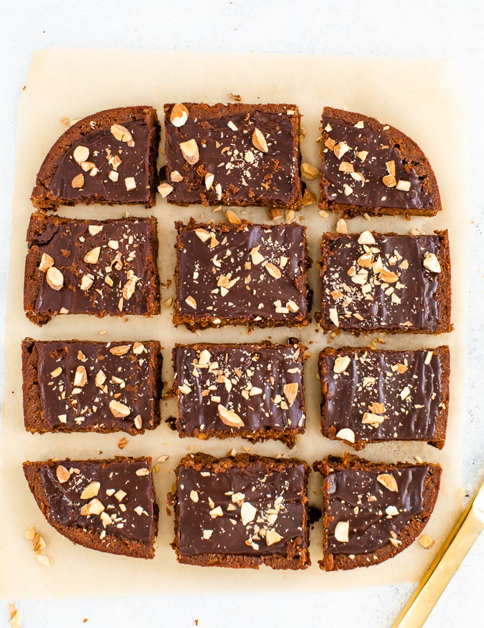 Sweet potato brownies on parchment paper topped with a chocolate ganache and chopped almonds.