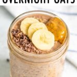 Glass jar filled with chocolate banana overnight oats and topped with cacao nibs, banana slices and a dollop of peanut butter.