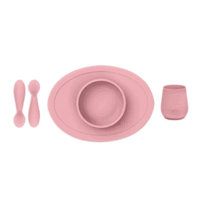 Blush colored ezpz First Food Set with two spoons, a bowl attached to a mat and tiny cup on a white background.