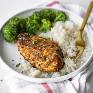 Grilled curry chicken on a plate with rice and broccoli.