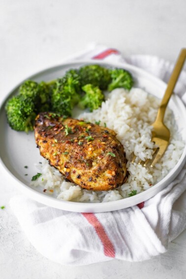 Grilled curry chicken on a plate with rice and broccoli.