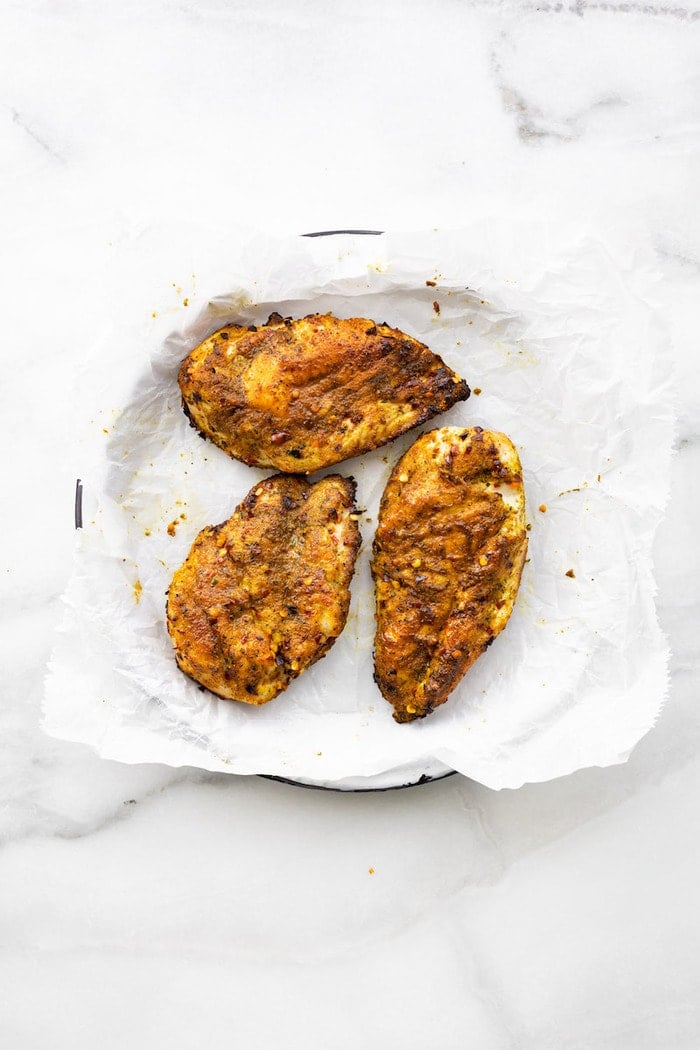 Three thai curry rubbed chicken breasts on a plate lined with paper.