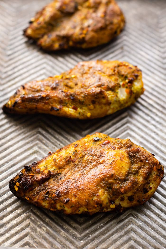 Three curry rubbed chicken breasts on a cookie sheet.