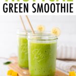 Two Ball mason jars filled with a green smoothie sitting on a wooden cutting board with mango chunks and spinach scattered around,
