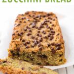 Loaf of chocolate chip zucchini bread on a cloth and cooking rack with one slice cut.