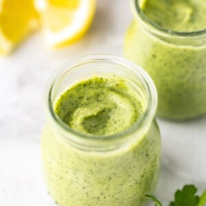 Two glass jars with avocado ranch dressing on a marble board with lemons in the background.