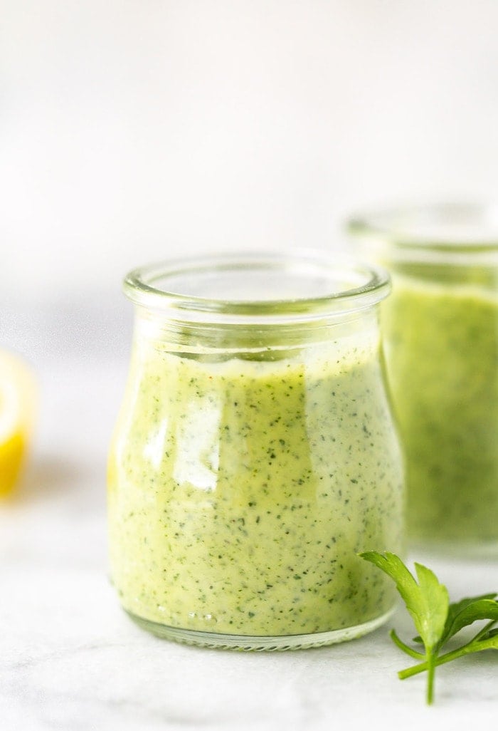 Straight on shot of two glass jars with avocado ranch dressing on a marble board.