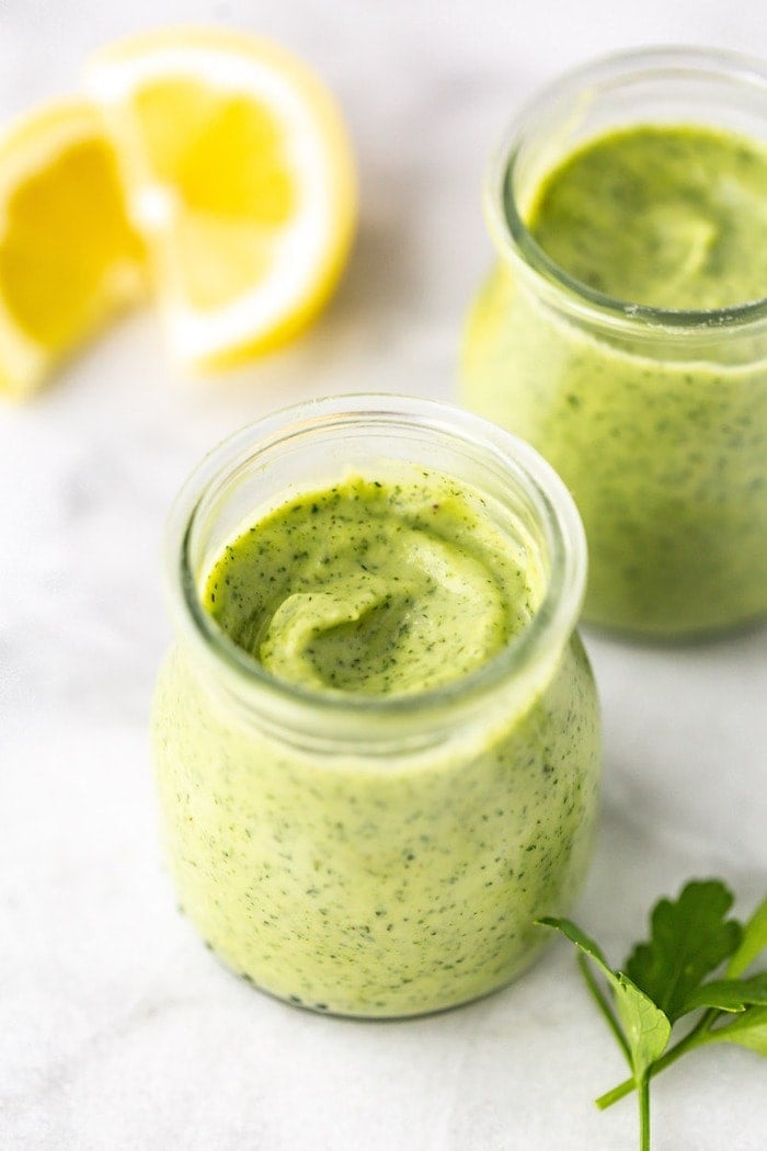 Two glass jars with avocado ranch dressing on a marble board with lemons in the background.