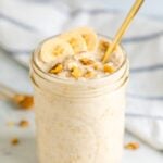 Mason jar with banana bread overnight oats, topped with banana slices and walnuts. Mason jar has a gold spoon handle sticking out.