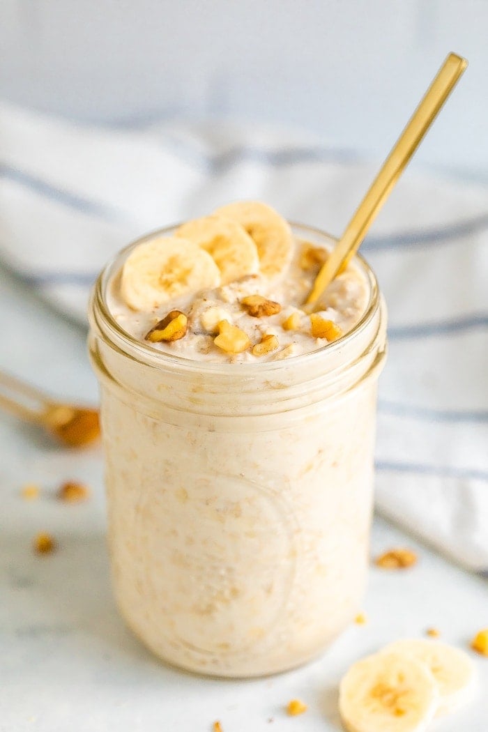 Mason jar with banana bread overnight oats, topped with banana slices and walnuts. Mason jar has a gold spoon handle sticking out.