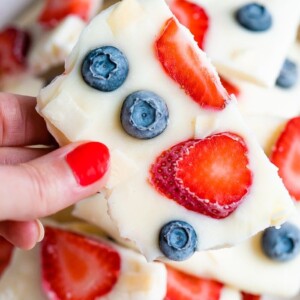 Hand holding a square of frozen yogurt bark topped with berries.