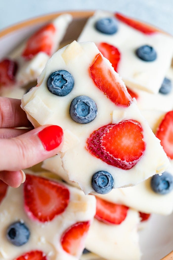 Hand holding a square of frozen yogurt bark topped with berries.