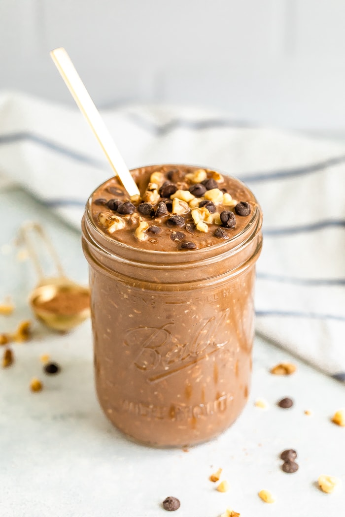 Brownie batter overnight oats in a mason jar with a gold spoon. Topped with walnuts and chocolate chips.