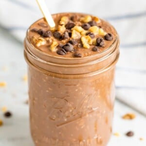Chocolate brownie batter overnight oats in a mason jar with a gold spoon. Topped with walnuts and chocolate chips.