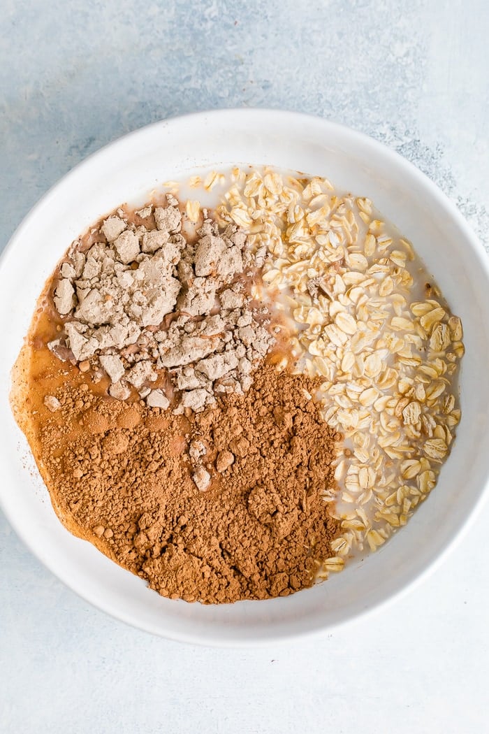 Ingredients for brownie batter overnight oats in a white bowl before mixing.