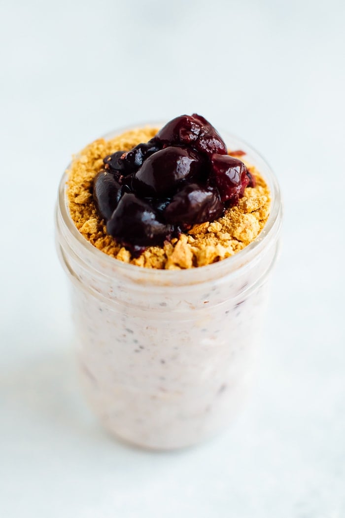 Cherry cheesecake overnight oats in a mason jar with graham cracker crumbs and cherries on top.