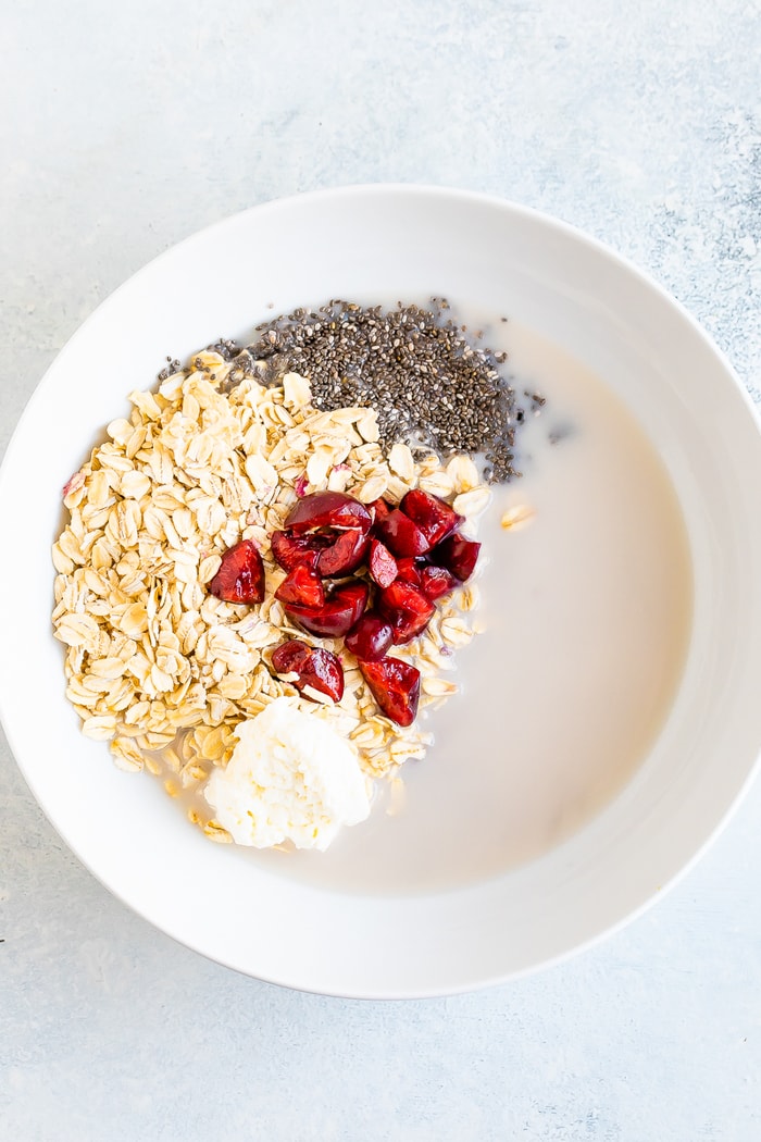 Ingredients for cherry cheesecake overnight oats in a white bowl before mixing.