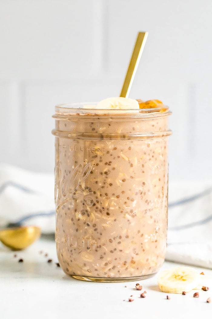 A mason jar with chocolate banana overnight oats with a gold spoon handling sticking out.