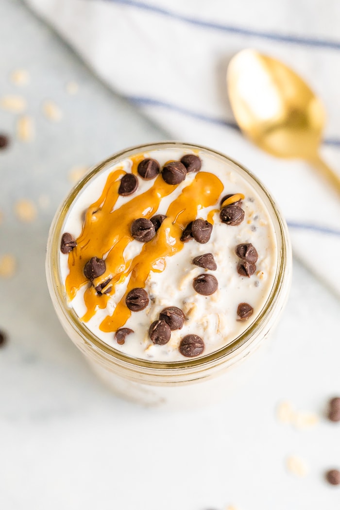 A serving of chocolate chip overnight oats in a mason jar. Topped with mini chocolate chips and a peanut butter drizzle.