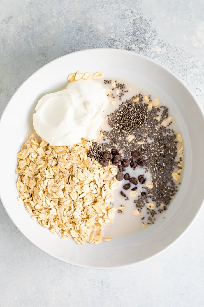 Ingredients for chocolate chip overnight oats in a white bowl before mixing.