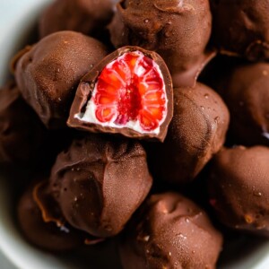 Bowl of chocolate covered frozen raspberries with yogurt. One raspberry is cut in half.