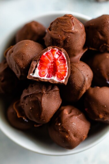 Bowl of chocolate covered frozen raspberries with yogurt. One raspberry is cut in half.