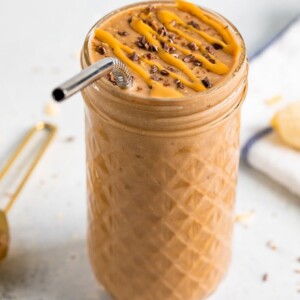 Glass jar with chocolate banana smoothie topped with cacao nibs and a peanut butter drizzle.