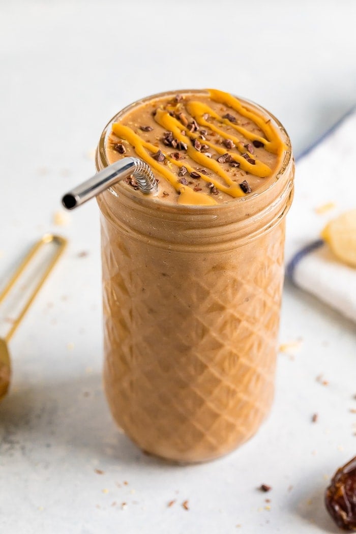 Glass jar with chocolate banana smoothie topped with cacao nibs and a peanut butter drizzle.