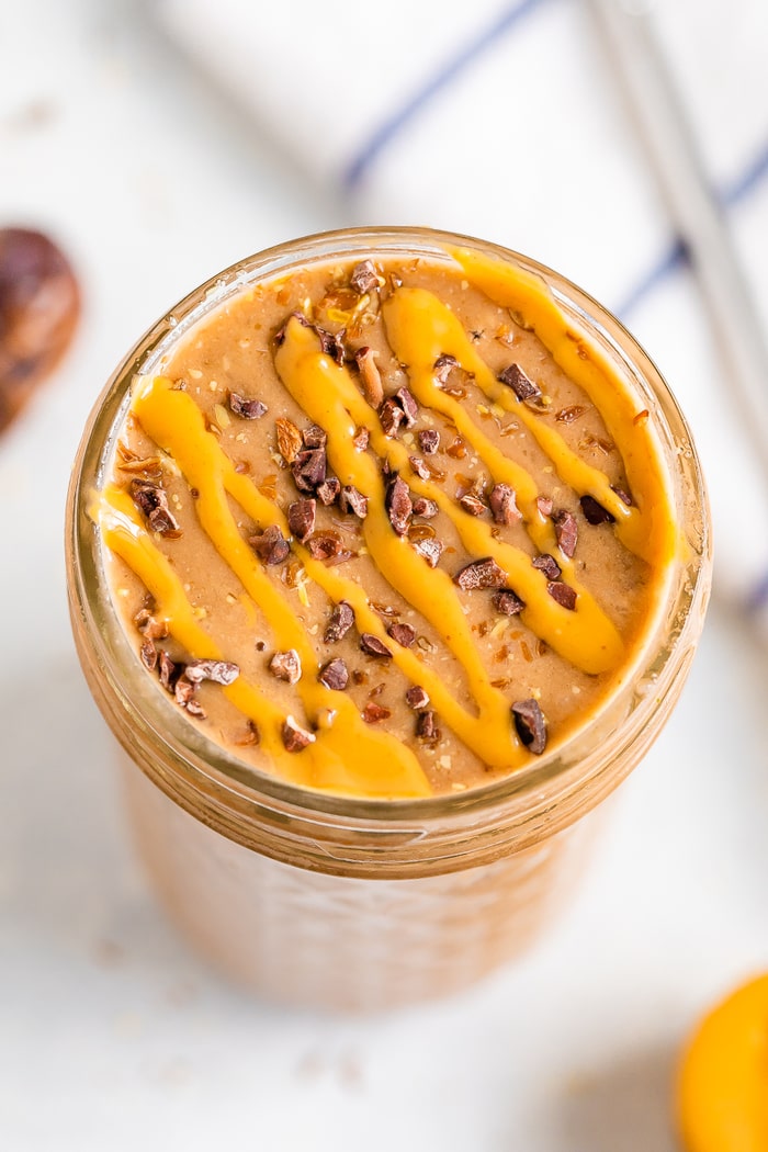 Glass jar with chocolate banana smoothie topped with cacao nibs and a peanut butter drizzle.