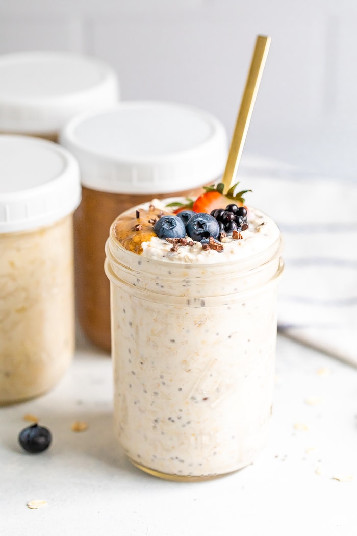 Basic overnight oats in a mason jar with a gold spoon. Several more jars behind the open jar with lids for meal prep.