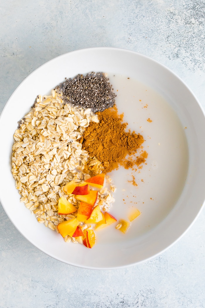 Ingredients for peach overnight oats in a white bowl before mixing.