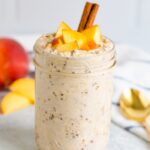 Peach overnight oats in a mason jar with fresh chopped peaches on top and a cinnamon stick.