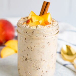 Peach overnight oats in a mason jar with fresh chopped peaches on top and a cinnamon stick.