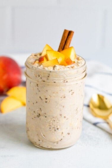 Peach overnight oats in a mason jar with fresh chopped peaches on top and a cinnamon stick.