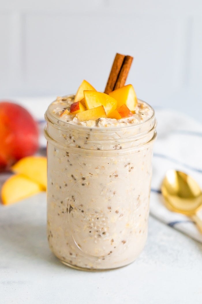 Peach overnight oats in a mason jar with fresh chopped peaches on top and a cinnamon stick.